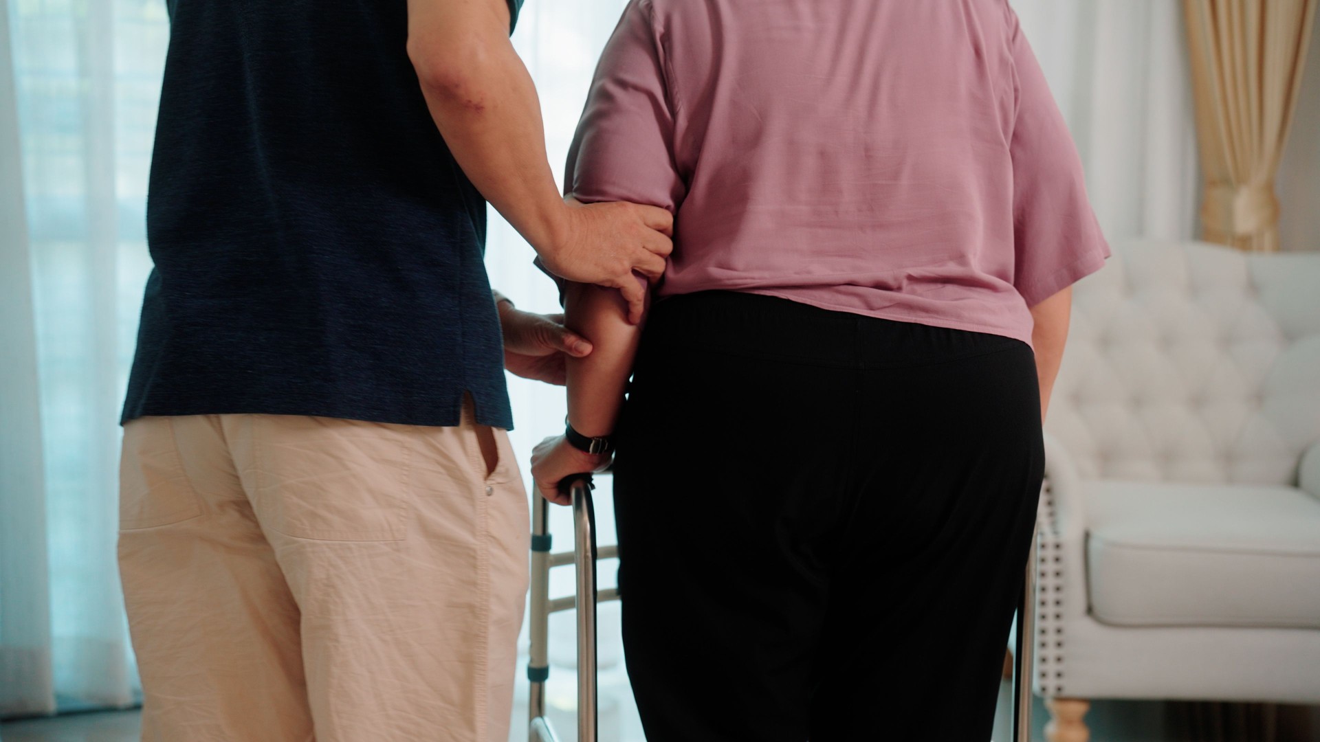 Couple of seniors helping each other, using a walker to reach the sofa