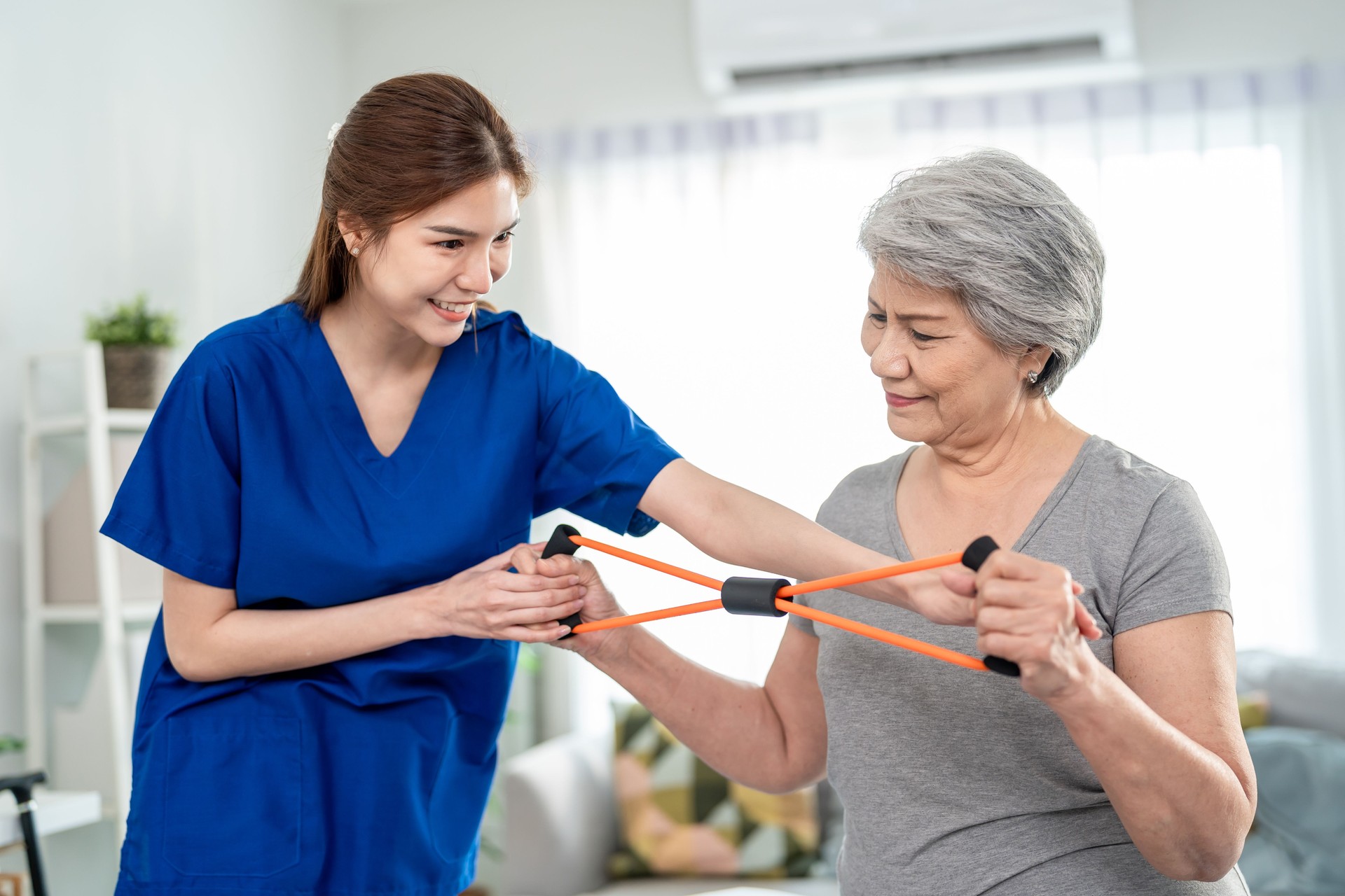 Elderly Asian woman receive physical therapy with support of caregiver. Senior patient engaging in gentle exercise improve mobility and strength under guidance of nurse therapist in nursing home care.